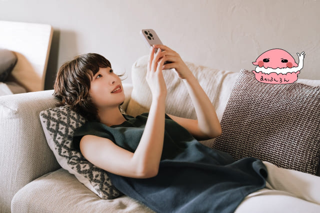 ソファーにあおむけになりスマホを操作する女性