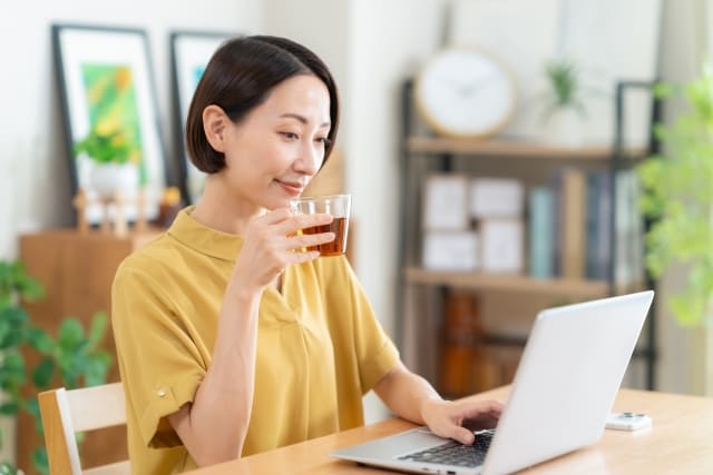 片手でドリンクを飲みながらPC操作する女性