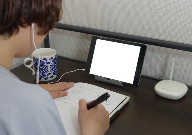 イヤホンをしてタブレットで勉強する人物