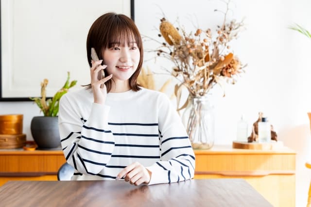 笑顔で電話をかけるストライプのトップスを来た女性